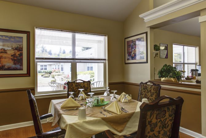 A cozy dining room with a neatly set table, featuring elegant decor and a large window allowing natural light to brighten the space.
