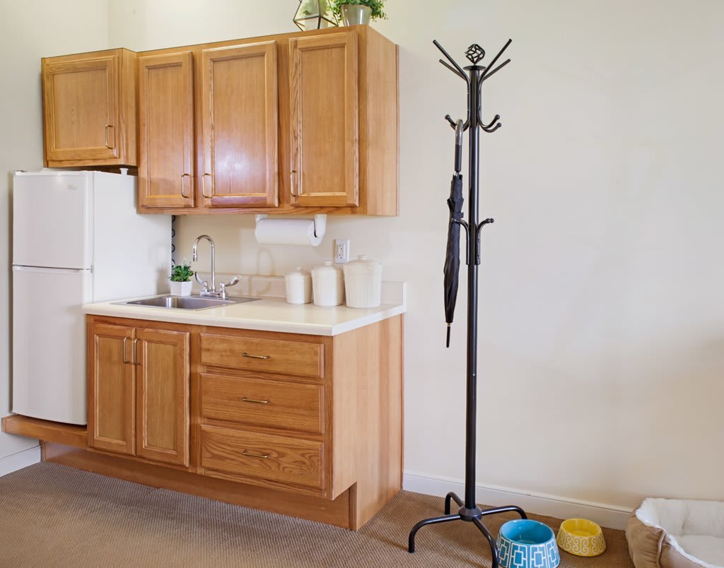 A kitchen area with wooden cabinets and a coat rack holding an umbrella.
