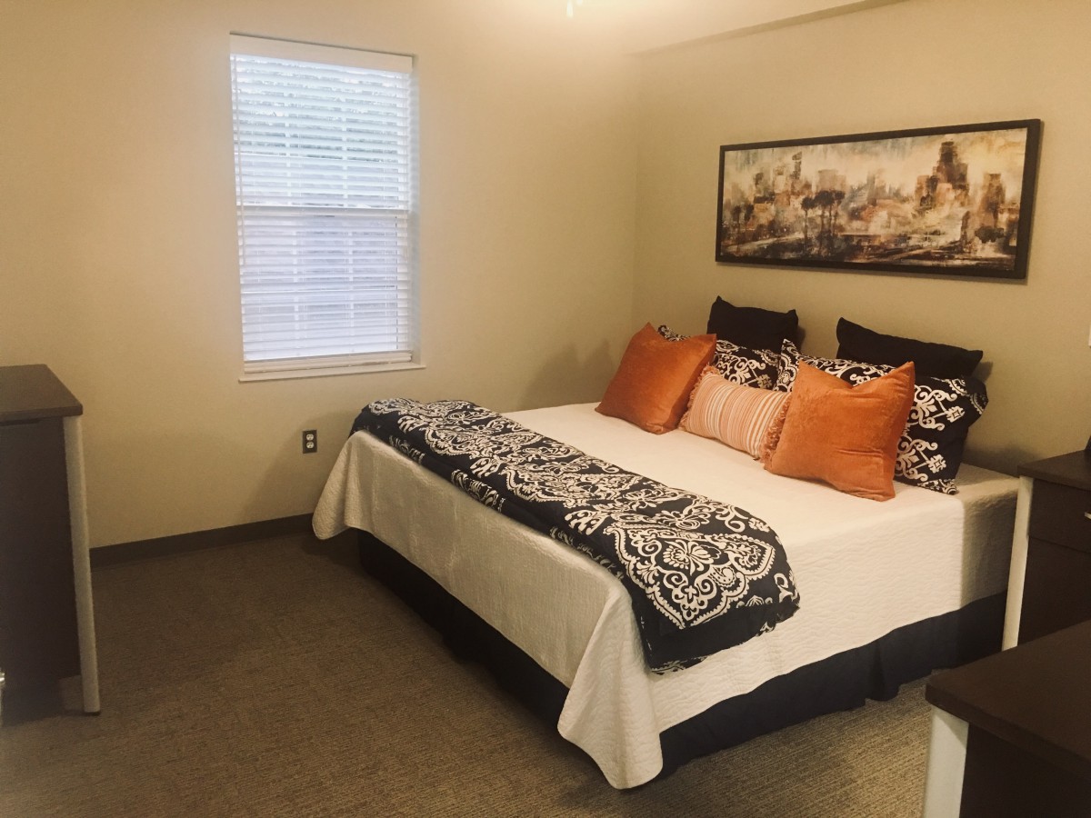 A cozy bedroom with a well-decorated bed, featuring vibrant pillows and wall art.