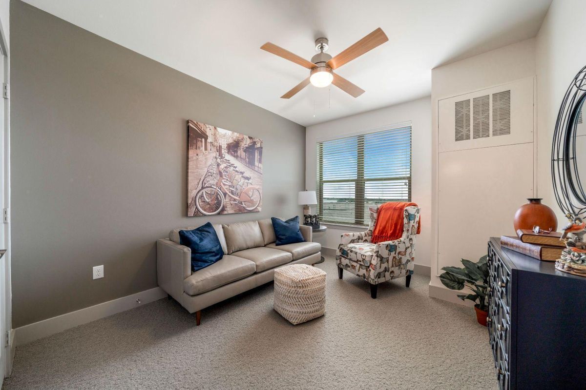 A cozy living room with a sofa, armchair, and ceiling fan in a bright space.