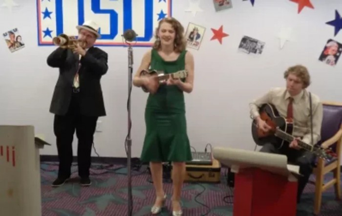 A band performing with a trumpet, ukulele, and guitar during a vintage-themed event.
