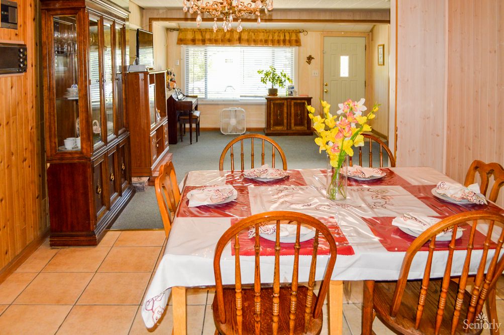 A cozy dining room with a wooden table set for four, adorned with a floral centerpiece and surrounded by matching chairs, beneath a chandelier.