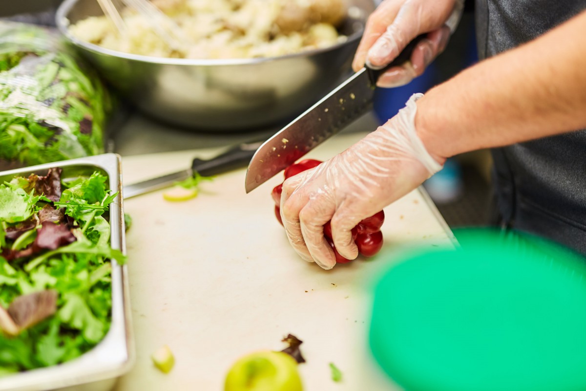 A person wearing gloves chops vegetables with a knife in a kitchen.