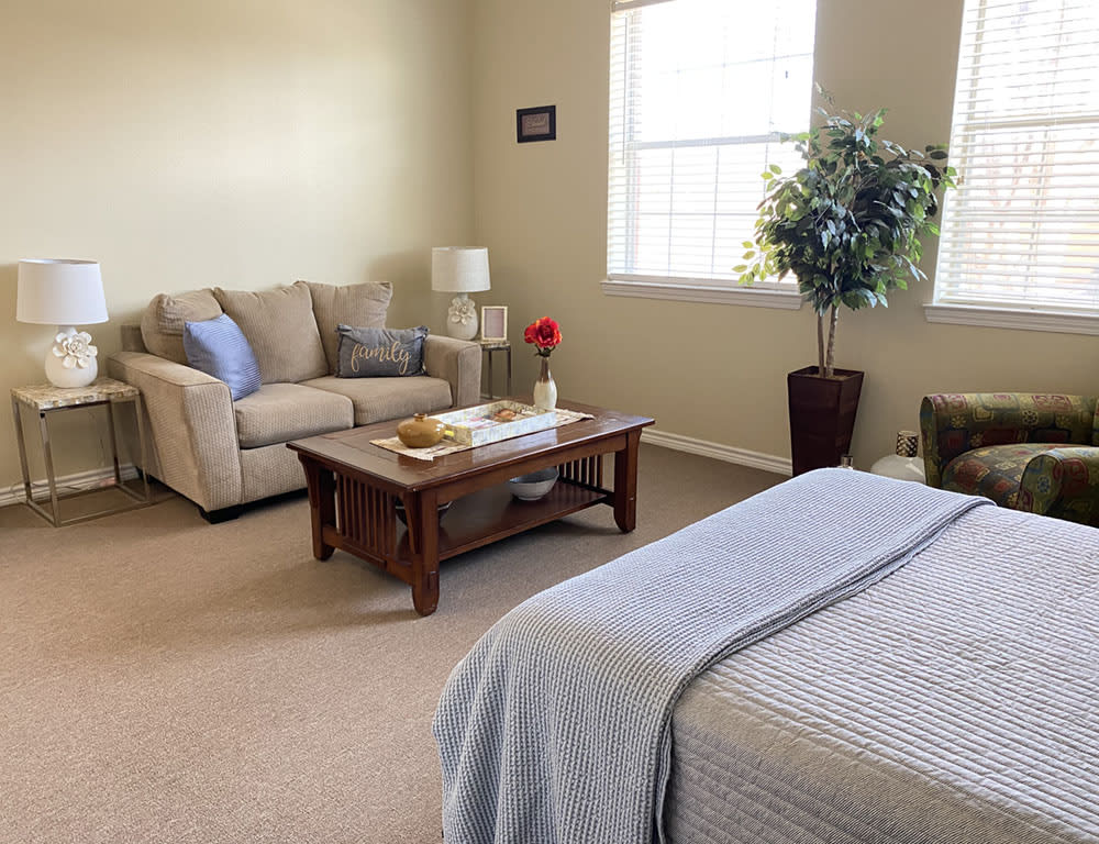A cozy bedroom with a seating area, featuring a couch, coffee table, and bed with light decor.