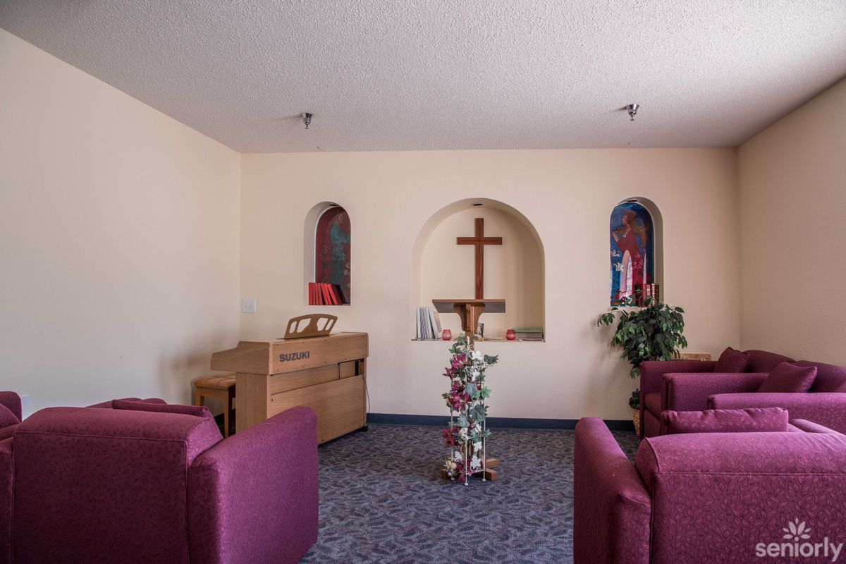 A small chapel with seating, a wooden cross, and two alcoves housing religious figures.