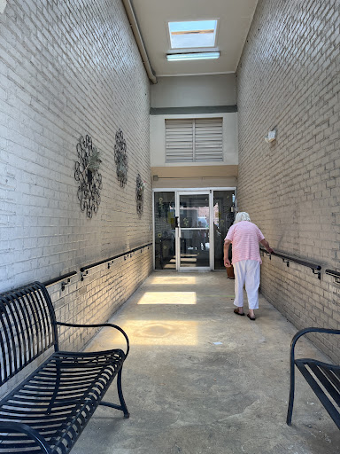 An elderly person walking towards the entrance of a well-lit hallway with benches on either side.