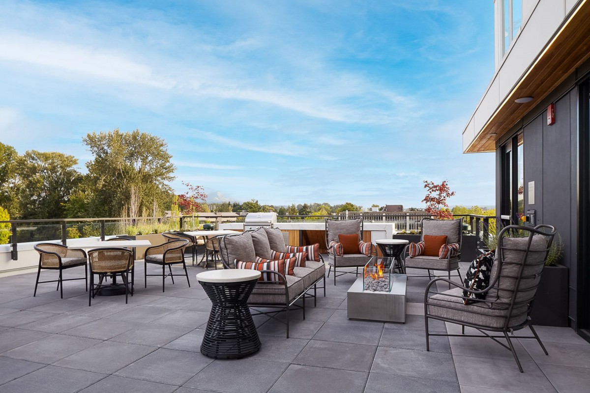 Modern outdoor patio with comfortable seating and a central firepit, set against a scenic landscape.