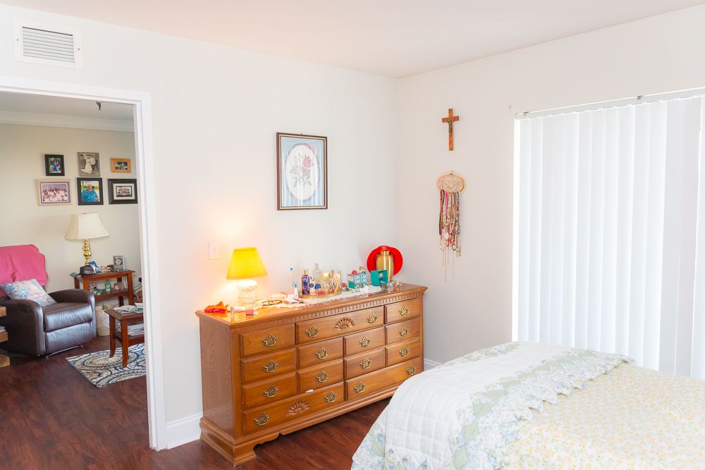 A cozy bedroom with a wooden dresser, illuminated by a small lamp and adorned with religious decor.