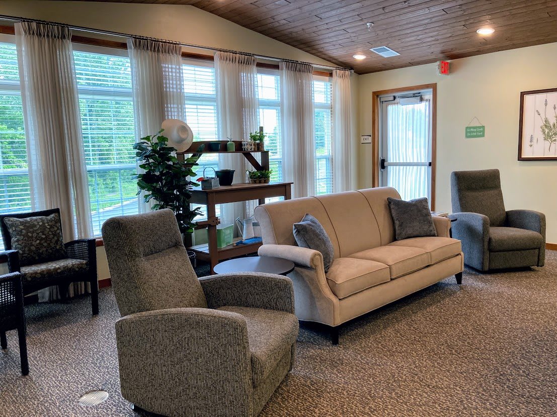 A cozy living room with comfortable seating, large windows allowing natural light, and lush green plants adding a touch of nature.