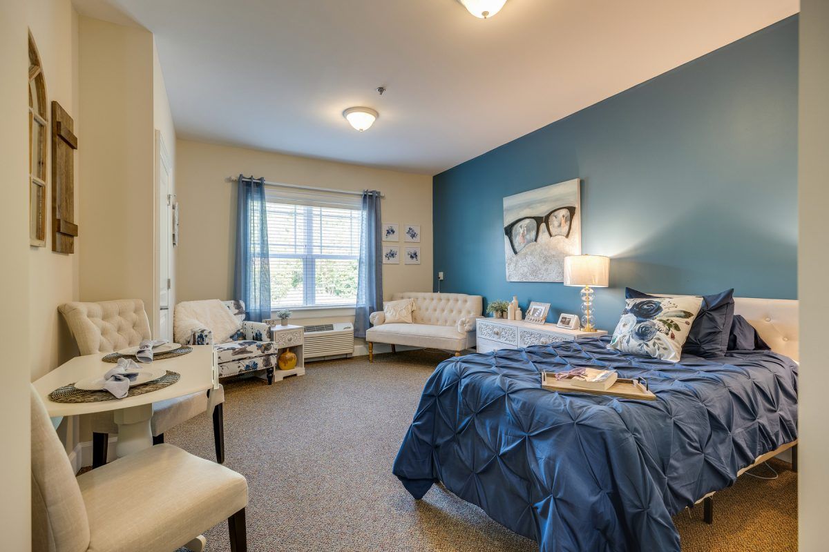A cozy and well-decorated bedroom with blue accents, featuring a bed, sofa, and ample natural light.