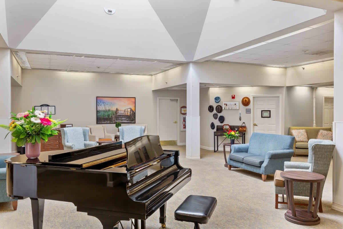 A spacious living room with a grand piano, comfortable seating, and decorative artwork.