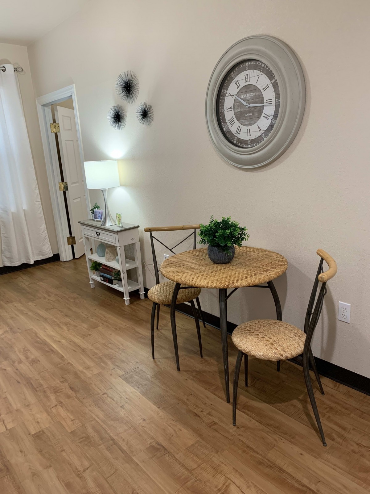 Cozy dining nook with a small table and chairs, accented by a wall clock and indoor plant.