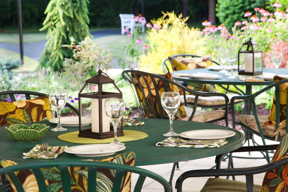 An inviting outdoor dining setup featuring tables with elegant place settings and lanterns, surrounded by lush greenery.