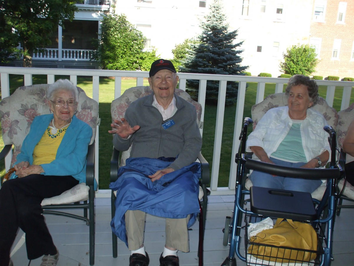 Three elderly women sitting on chairs outside on a porch.