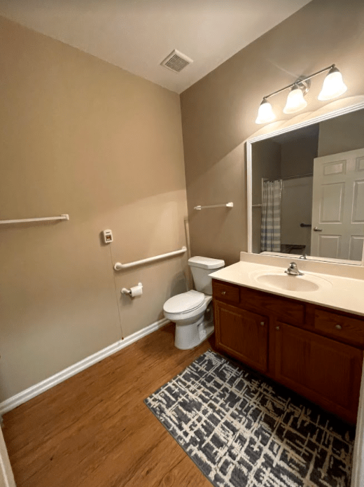 A well-lit bathroom with a vanity, sink, and toilet on hardwood flooring.