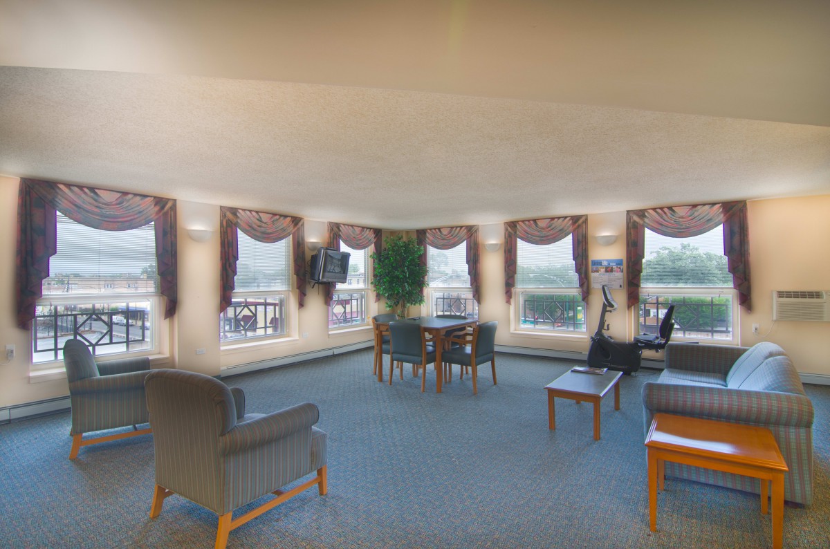 A spacious lounge area with multiple windows, decorated with comfortable seating and tables.