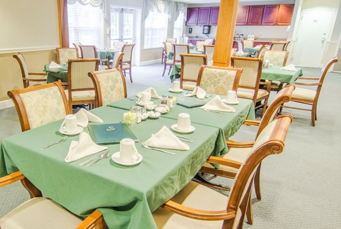 Elegantly set dining tables with green tablecloths in a cozy restaurant setting.