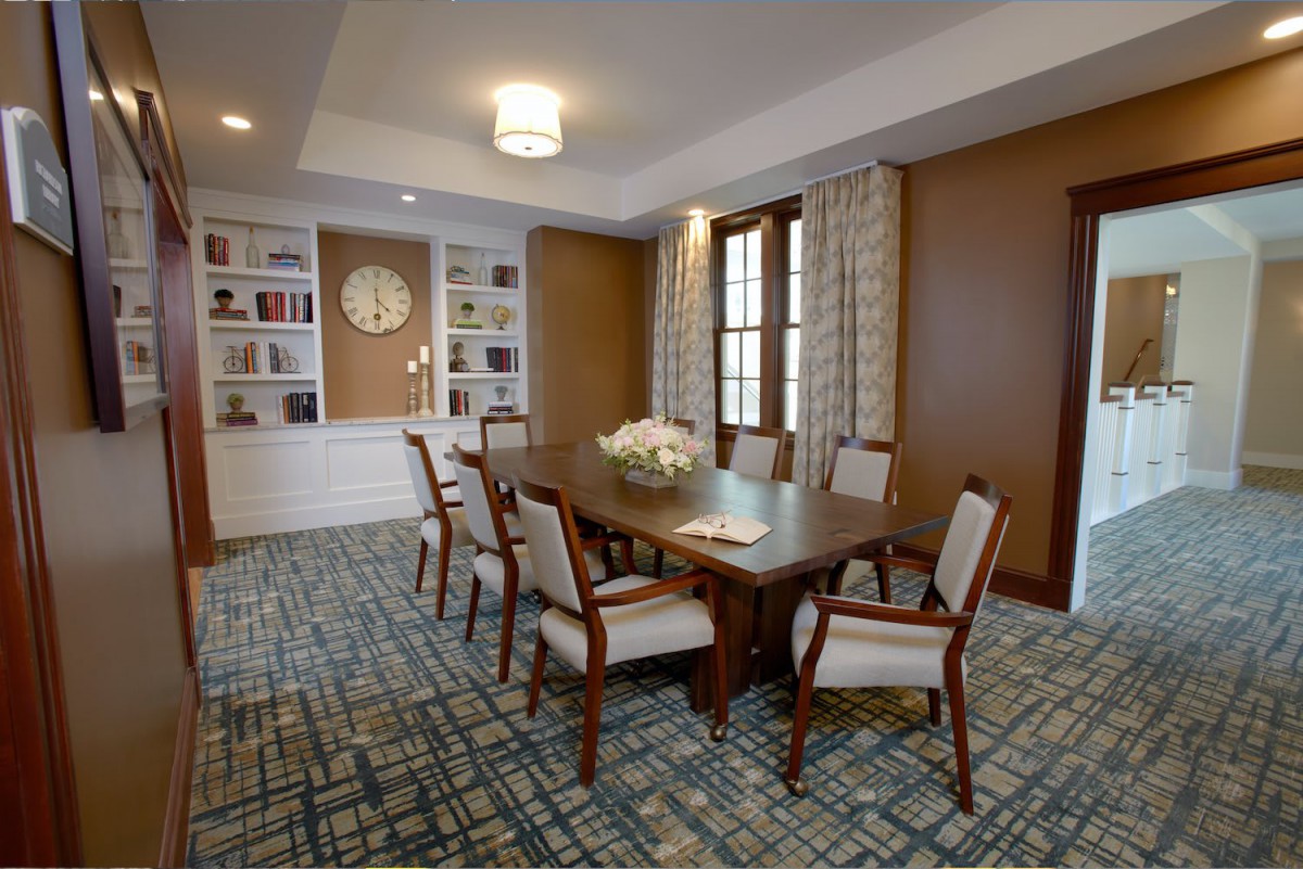A well-appointed meeting room with a large conference table and chairs, flanked by bookshelves and elegant decor.