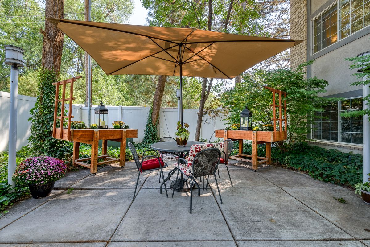 A cozy patio setup with a large umbrella, garden furniture, and lush greenery.
