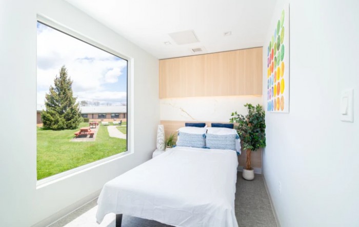 A minimalist bedroom with a large window offering a scenic view, featuring modern decor and natural light.