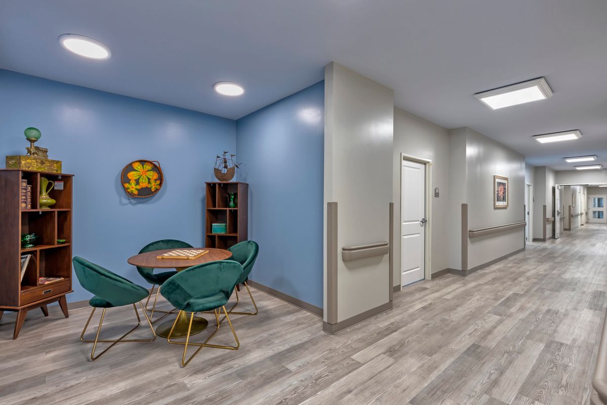 A cozy indoor space featuring a seating area with green chairs and a round table, set against blue walls and wooden flooring.