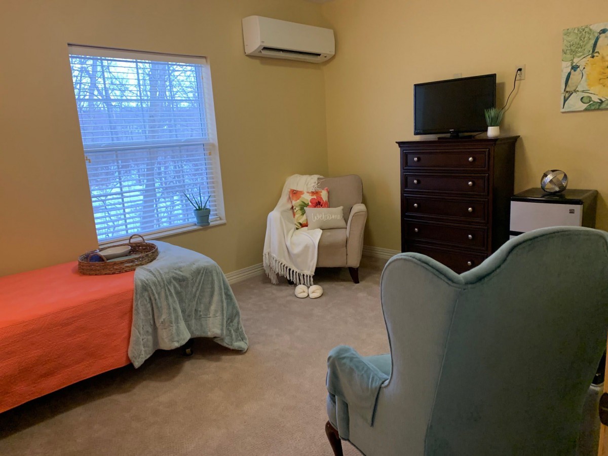 A cozy bedroom with a bed, armchair, dresser, and TV.