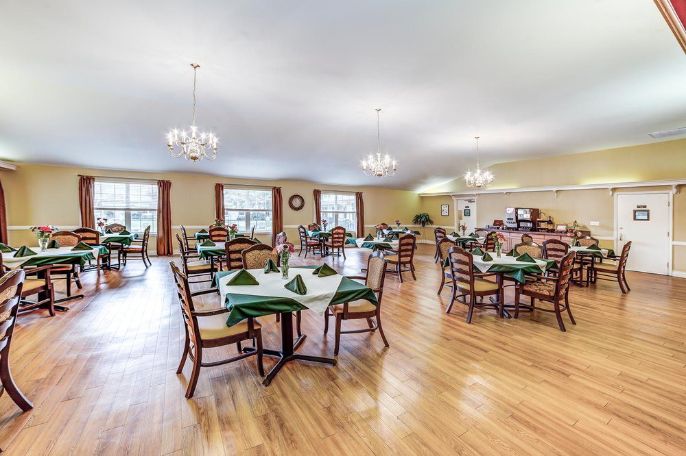 An elegant dining hall with neatly arranged tables and chairs, featuring chandeliers and a bright atmosphere.