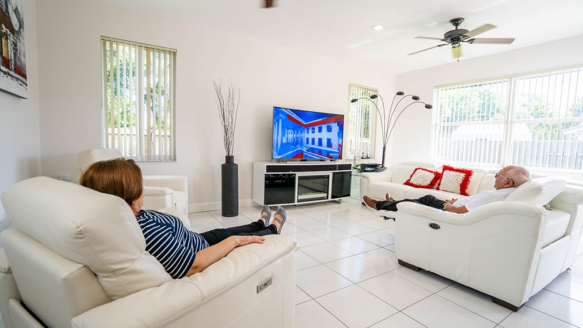 A modern living room with people relaxing on white sofas, watching television.