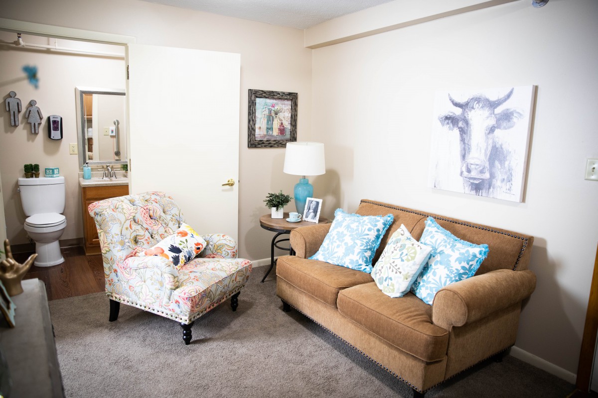 A cozy living room with a brown sofa and floral armchair, accented by decorative pillows and artwork.