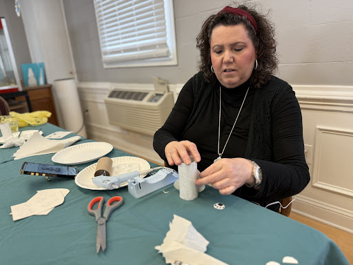 A woman focused on a crafting project, using scissors and various materials at a table.
