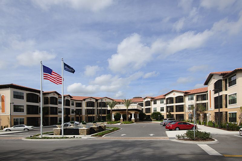 A hotel with a parking lot and flags flying under a cloudy sky.