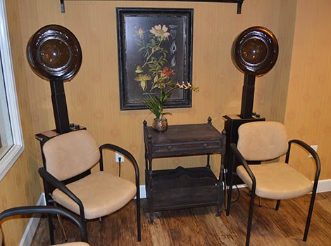 A cozy salon waiting area with chairs and hair dryers, featuring a floral painting on the wall.