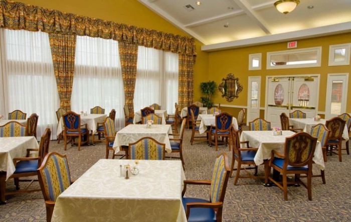 An empty dining room with neatly arranged tables and chairs, featuring large windows with curtains.