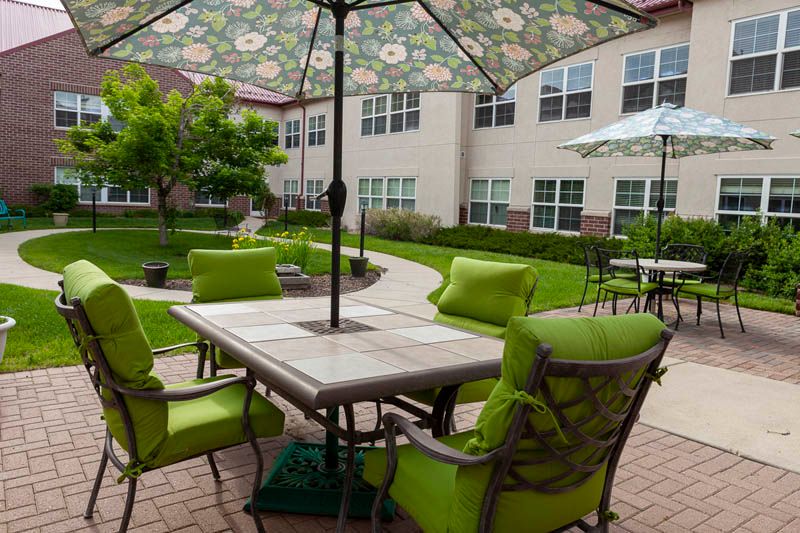 An inviting outdoor patio with green-cushioned chairs and floral umbrellas in a residential courtyard.