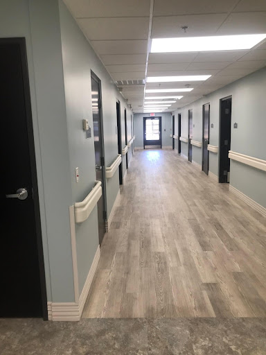 A well-lit hallway in a healthcare facility, featuring multiple doors and modern flooring.