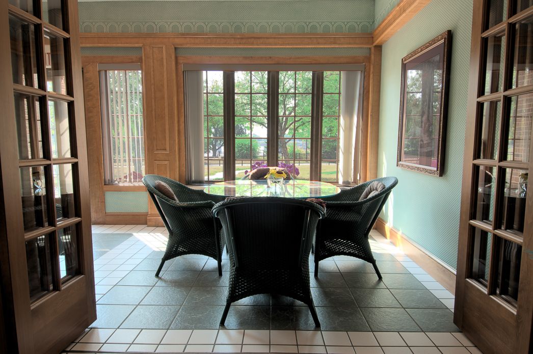 A cozy dining area with a round table surrounded by four chairs, bathed in natural light from large windows.