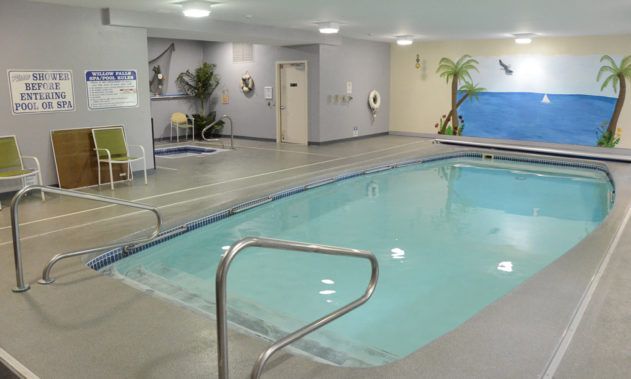 An indoor swimming pool area equipped with safety features and decorated with a beach-themed mural.