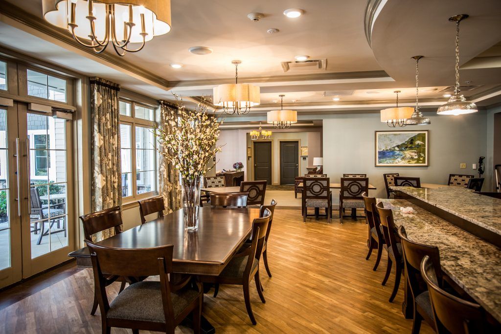 A well-appointed dining room featuring a large wooden table, numerous chairs, elegant chandeliers, and decorative curtains.