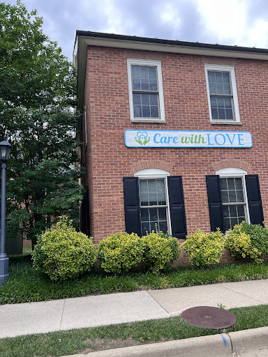 A brick building featuring a sign that reads 'Currents of Love' surrounded by lush greenery.