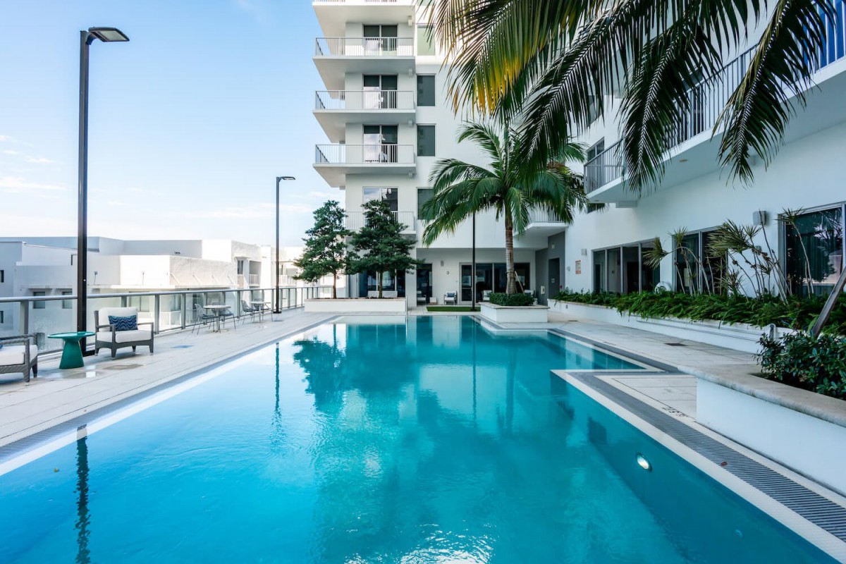 A modern apartment building with an outdoor swimming pool surrounded by palm trees.