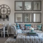 A stylish living room with a tufted sofa, decorative cushions, and mirrored wall art.