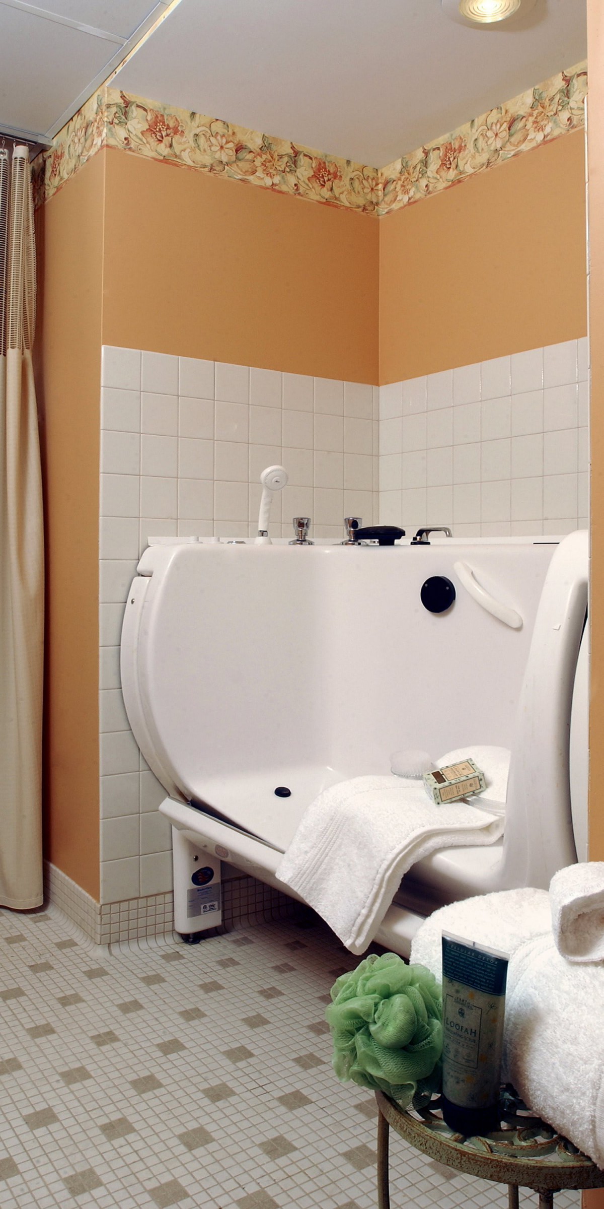 An accessible bathtub featuring a side door, set in a tiled bathroom with towels and a showerhead.