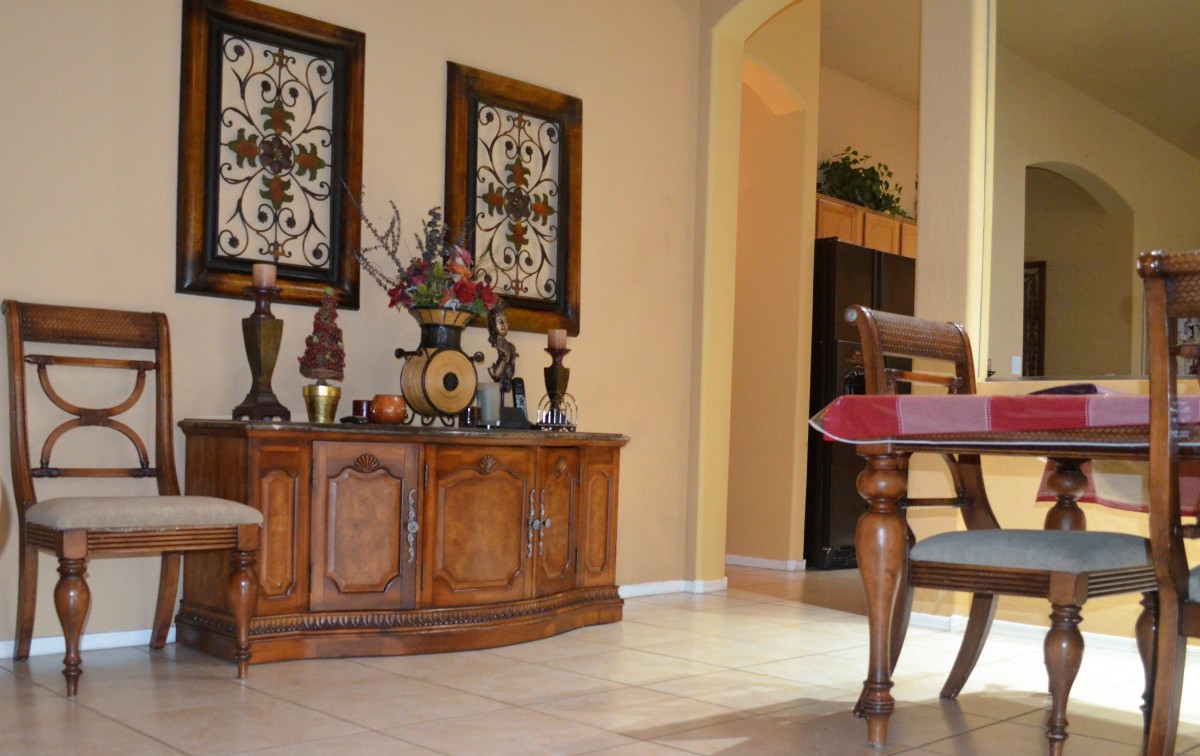 A cozy living room interior featuring a wooden cabinet adorned with vases and artwork, alongside a partially visible dining table.