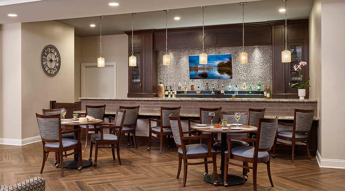 A modern restaurant interior with a bar, featuring tables and chairs, pendant lighting, and wood flooring.