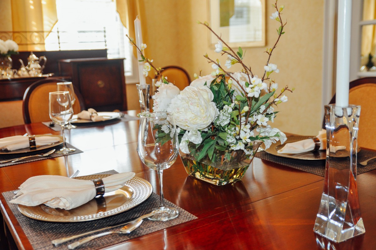 A beautifully set dining table featuring a floral centerpiece with white flowers and elegant place settings.
