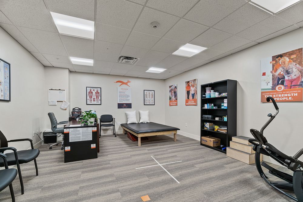 A therapy or rehabilitation room equipped with various exercise tools, posters on the wall, and a set of shelves filled with materials.