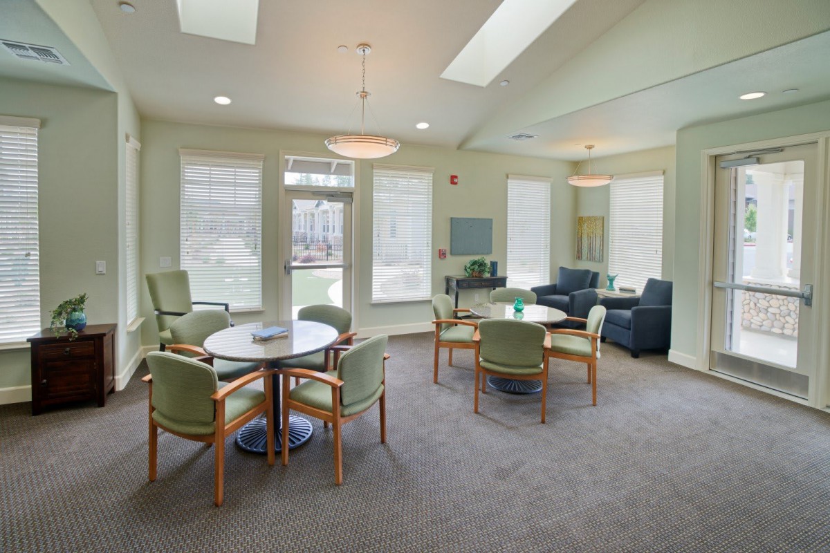 A cozy living area with tables, chairs, and sofas, featuring large windows.
