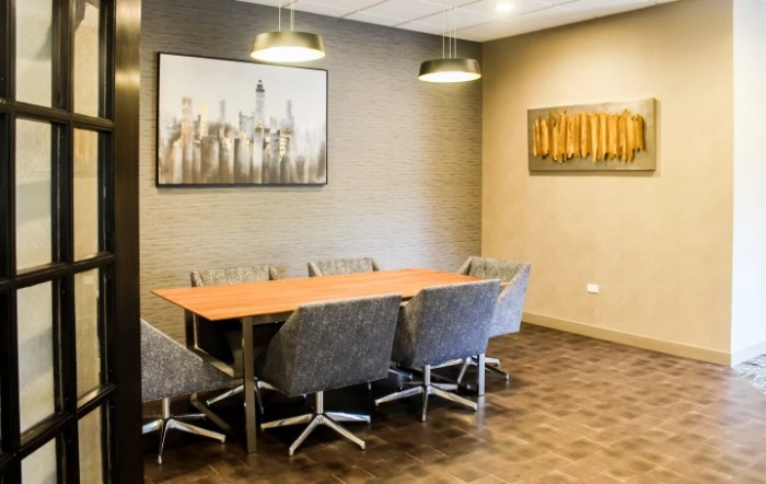 A modern conference room featuring a wooden meeting table surrounded by office chairs, adorned with contemporary artwork on the walls.