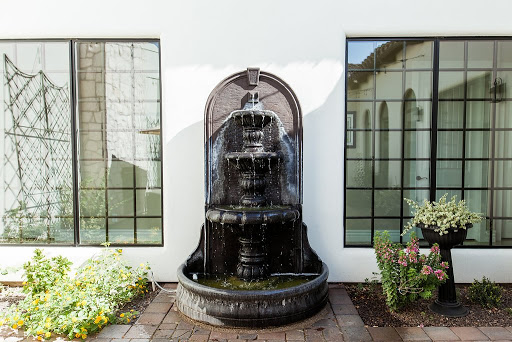 A beautiful outdoor fountain surrounded by greenery, framed by large windows.
