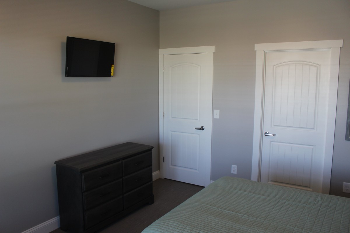 A bedroom with a wall-mounted TV, dresser, and two doors in neutral tones.